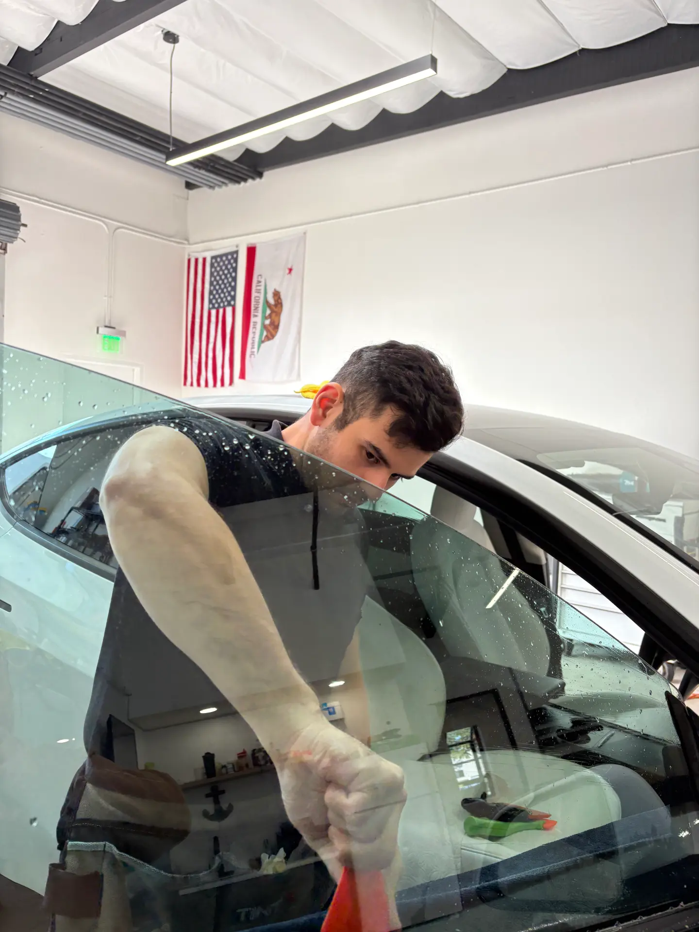 Installer squeegeeing tint film on a Tesla window inside the shop